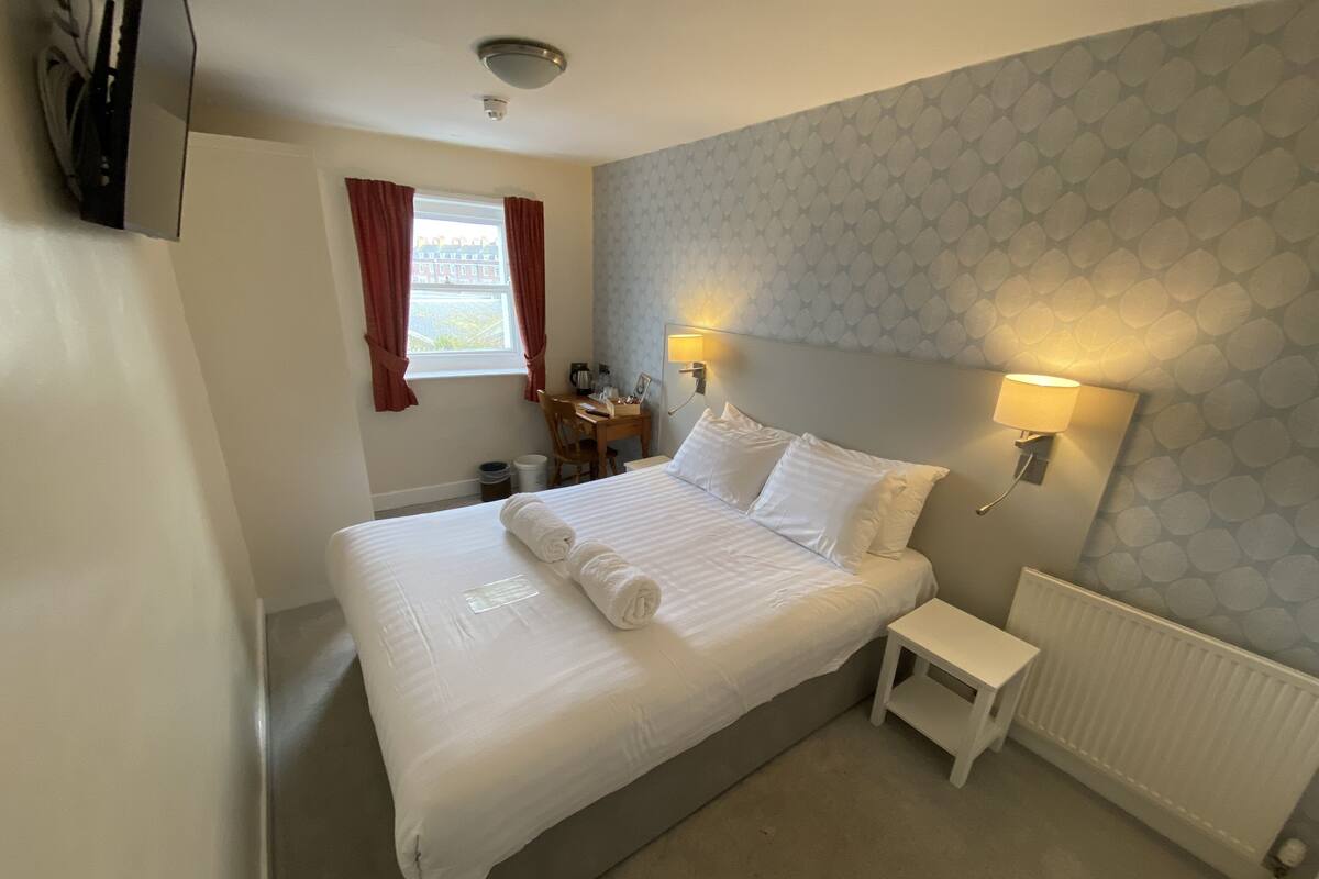 A hotel room with a large bed, bedside lamps, a small table, and a window with curtains.