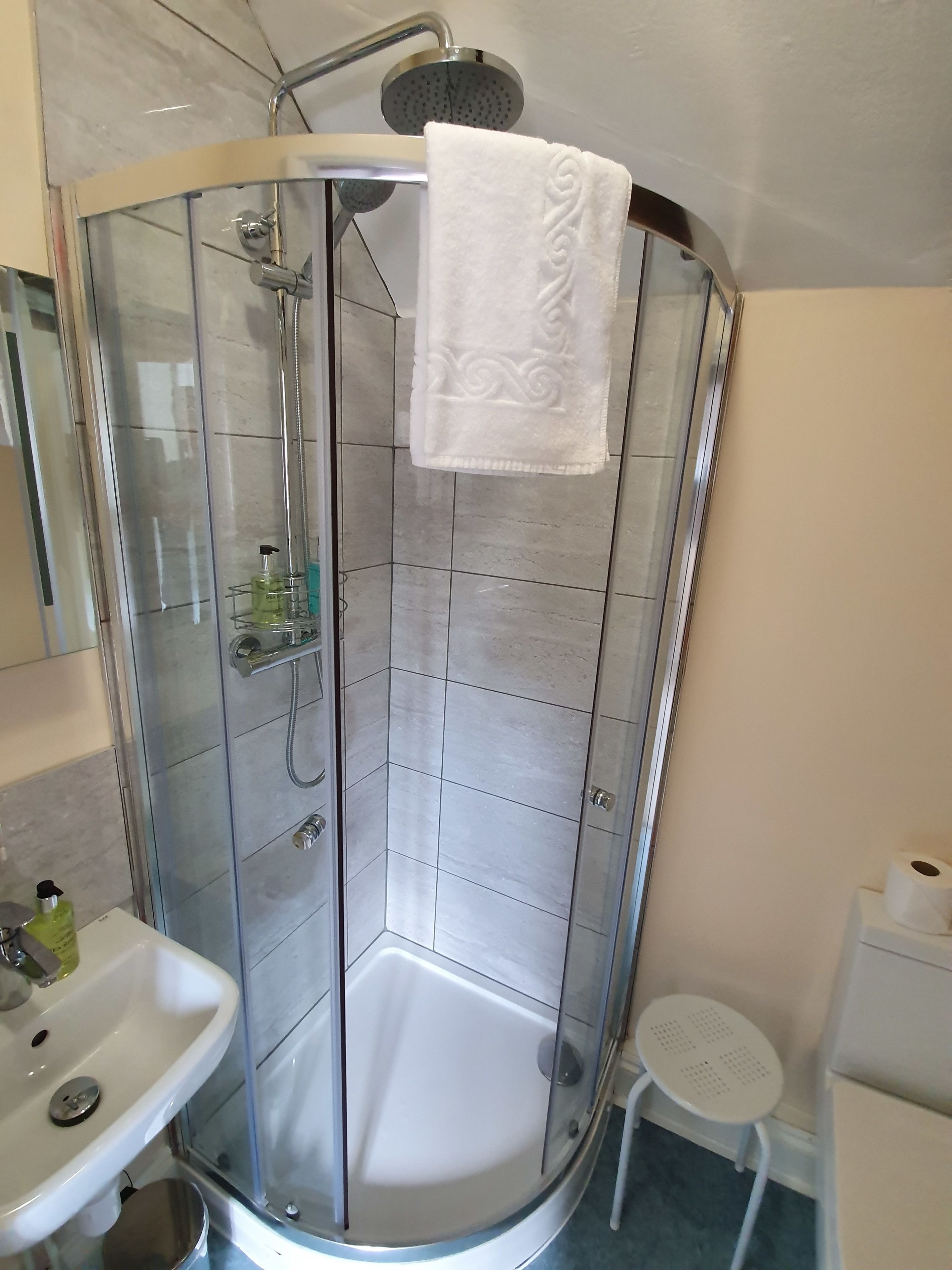 Ein modernes Badezimmer mit einer gläsernen Duschkabine, einem weißen Waschbecken und einem kleinen weißen Tisch.