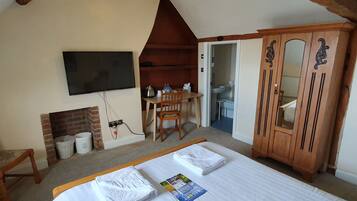 A bedroom with a large bed, a wooden wardrobe, a television mounted on the wall, and a small desk with a chair.