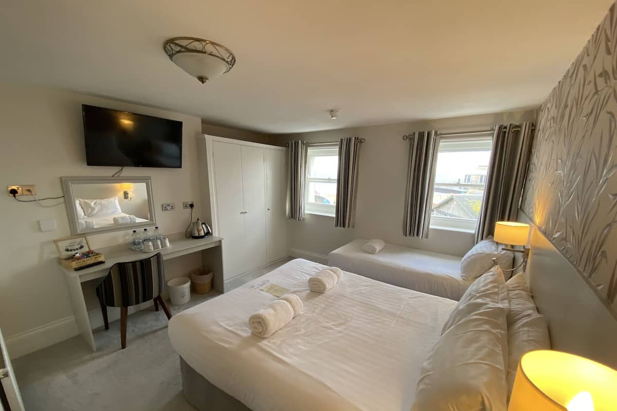 A hotel room with two beds, a desk with a mirror, a television, and a window with curtains.