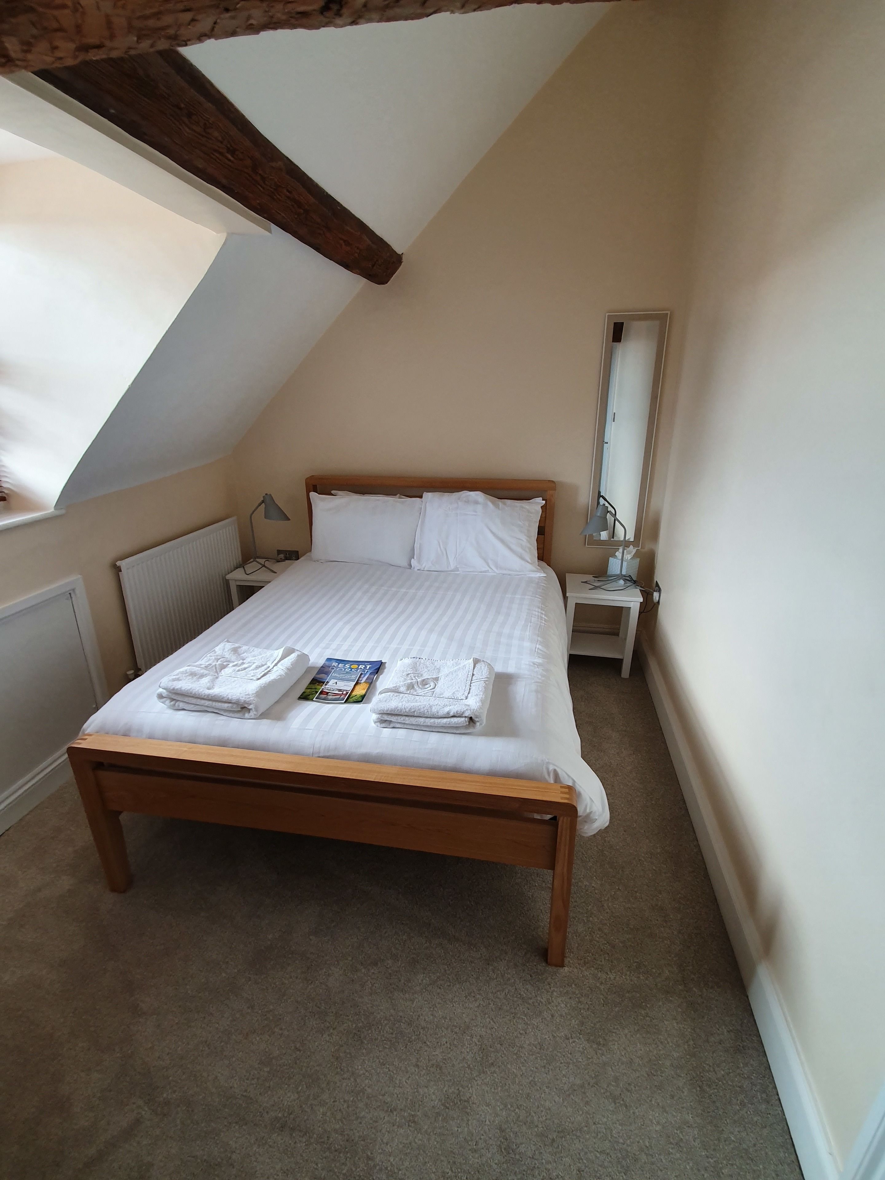 Une chambre à coucher avec un lit en bois, du linge de lit blanc, une table de chevet avec une lampe, un radiateur et une fenêtre donnant sur un beau paysage.