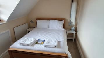 A bedroom with a wooden bed, white linens, a bedside table with a lamp, a radiator, and a window with a view.