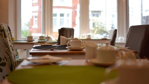 A dining area with a table set for two, a window with a view of buildings, and a chair with a floral pattern. - The Beaucliffe (Blackpool)