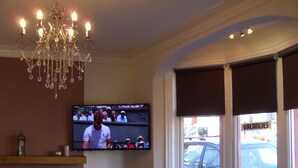 A room with a television displaying a sports event, a chandelier, a fireplace, and a window with a view of the street. - The Beaucliffe (Blackpool)