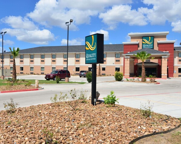 A Quality Inn & Suites hotel with a parking lot, palm trees, and a clear sky.