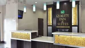 A reception area with two counters, each with a nameplate and a Dell computer. The walls have a dark wood finish with gold accents, and there are several pendant lights above the counters. - Quality Inn & Suites Kenedy - Karnes City (Kenedy)