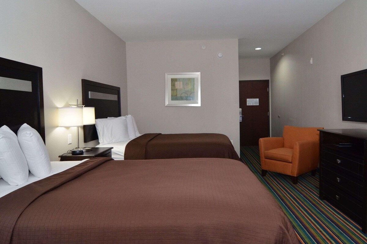 A hotel room with two beds, a desk with a lamp, a chair, a TV, and a dresser.