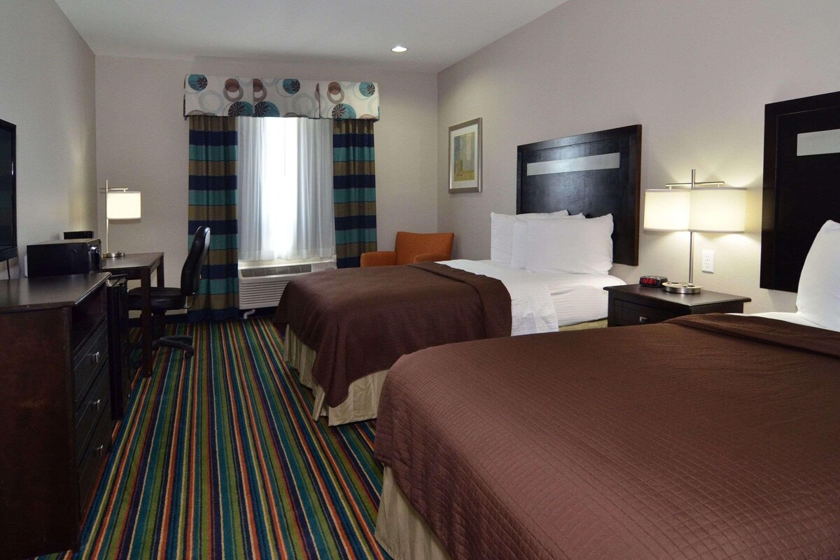 A hotel room with two beds, a desk with a chair, a television, and a window with curtains.