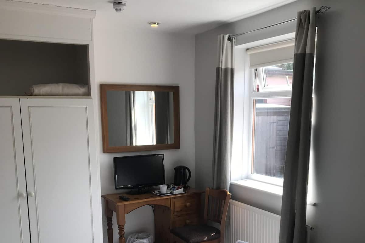 A hotel room with a bed, a desk with a chair, a television, and a wardrobe.