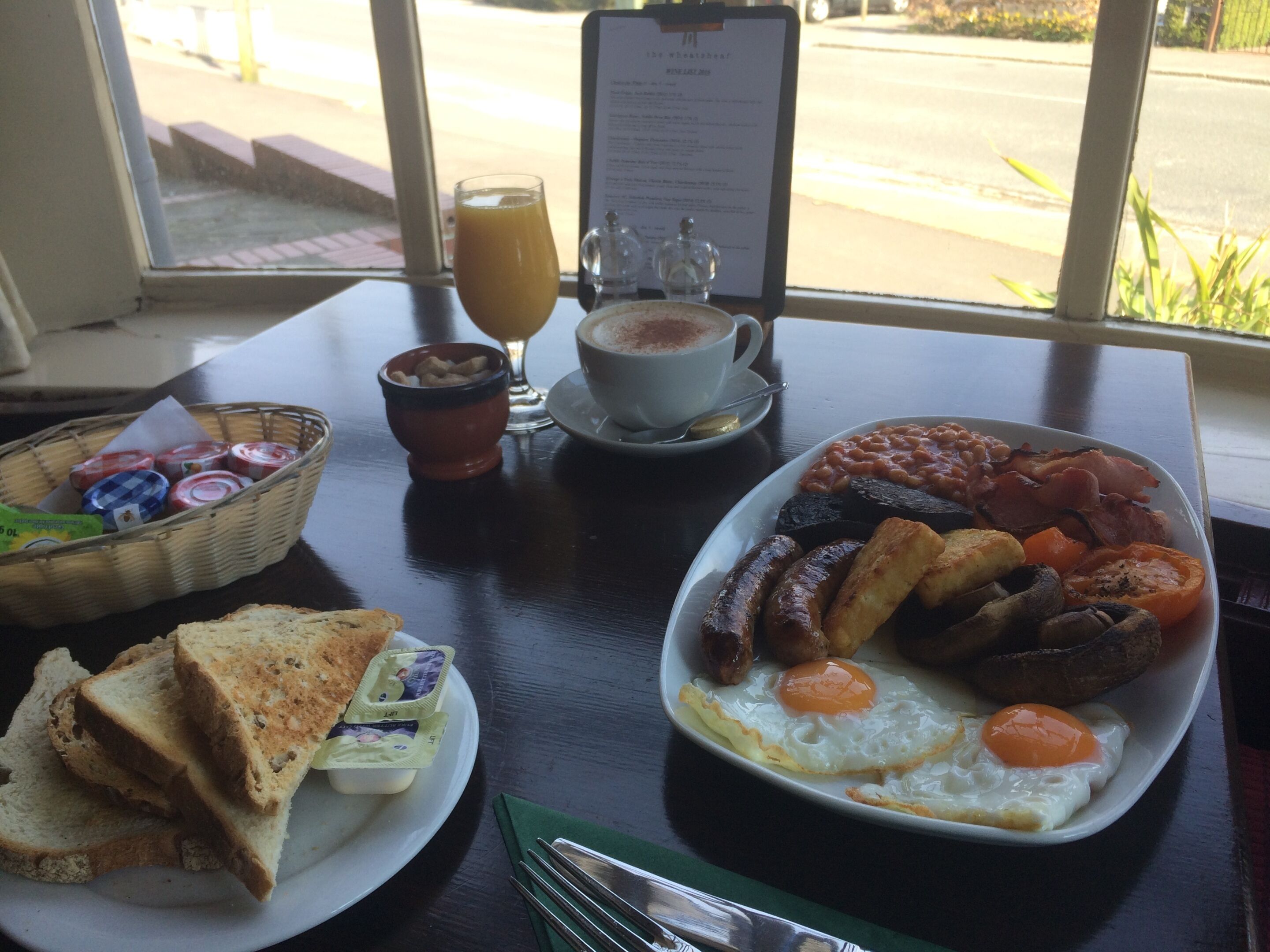 A breakfast table with toast, eggs, beans, bacon, and a drink.