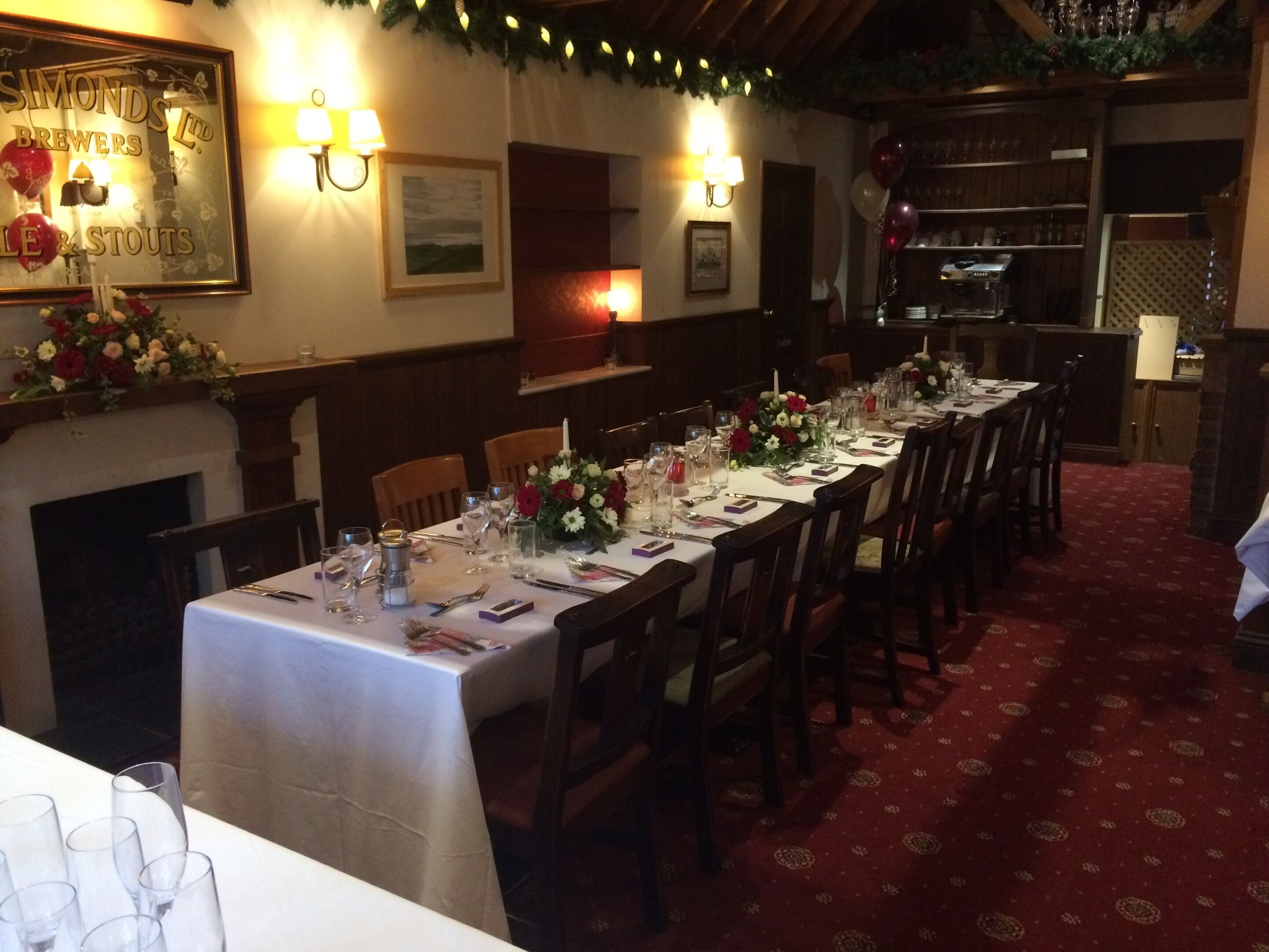 A restaurant with a long dining table set for a meal, wooden chairs, and a fireplace.