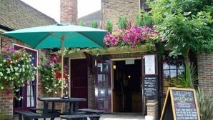 Un espace extérieur aménagé avec des tables et des bancs, un parasol vert et un panneau noir accueillant les visiteurs.