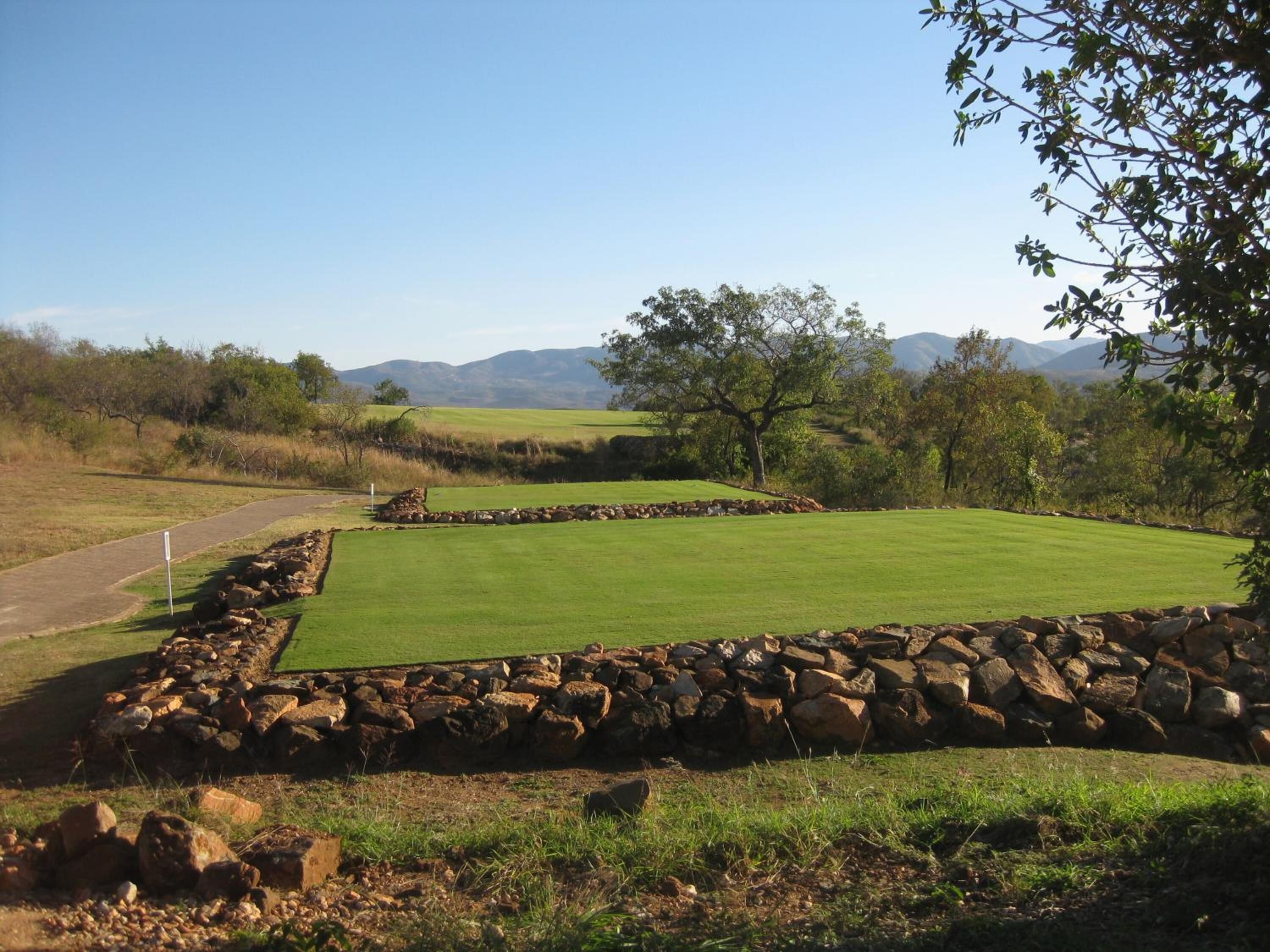 Un campo de golf con un green cuidado, muros de piedra y un camino despejado para jugar.