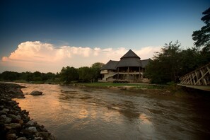 A riverside hotel with a prominent conical roof and a bridge leading to the entrance.