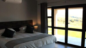 Een slaapkamer met een groot bed, een hoofdeinde, een bedlampje en uitzicht door een schuifdeur.
