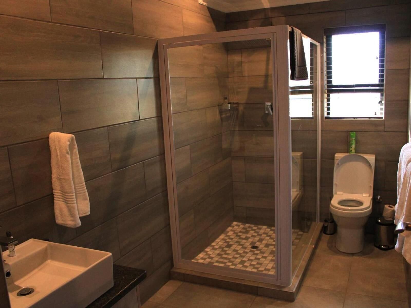 Un baño moderno con ducha separada por mampara de vidrio, inodoro y lavamanos.