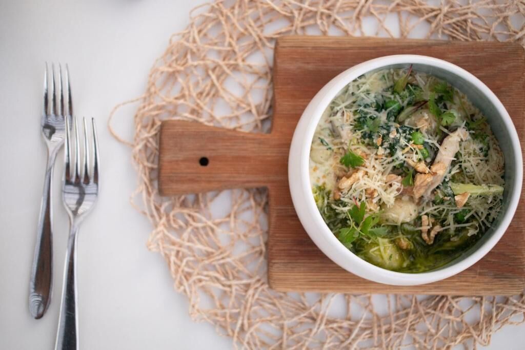 Eine Schüssel Nudelsuppe mit Hähnchen und Gemüse auf einer Holzplatte.