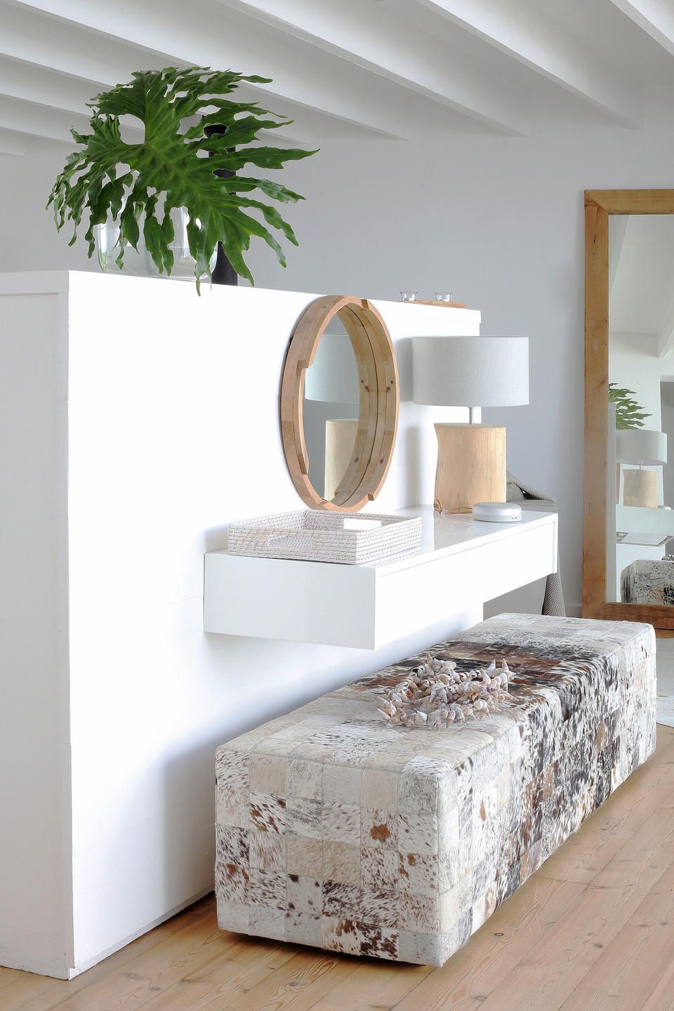 Et moderne badeværelse med et hvidt toiletbord, et rundt spejl, et spejl med træramme, en hvid lampe og en potteplante.