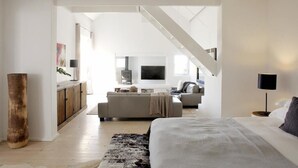 A modern bedroom with a large bed, a staircase leading to an upper level, and a minimalist decor style.