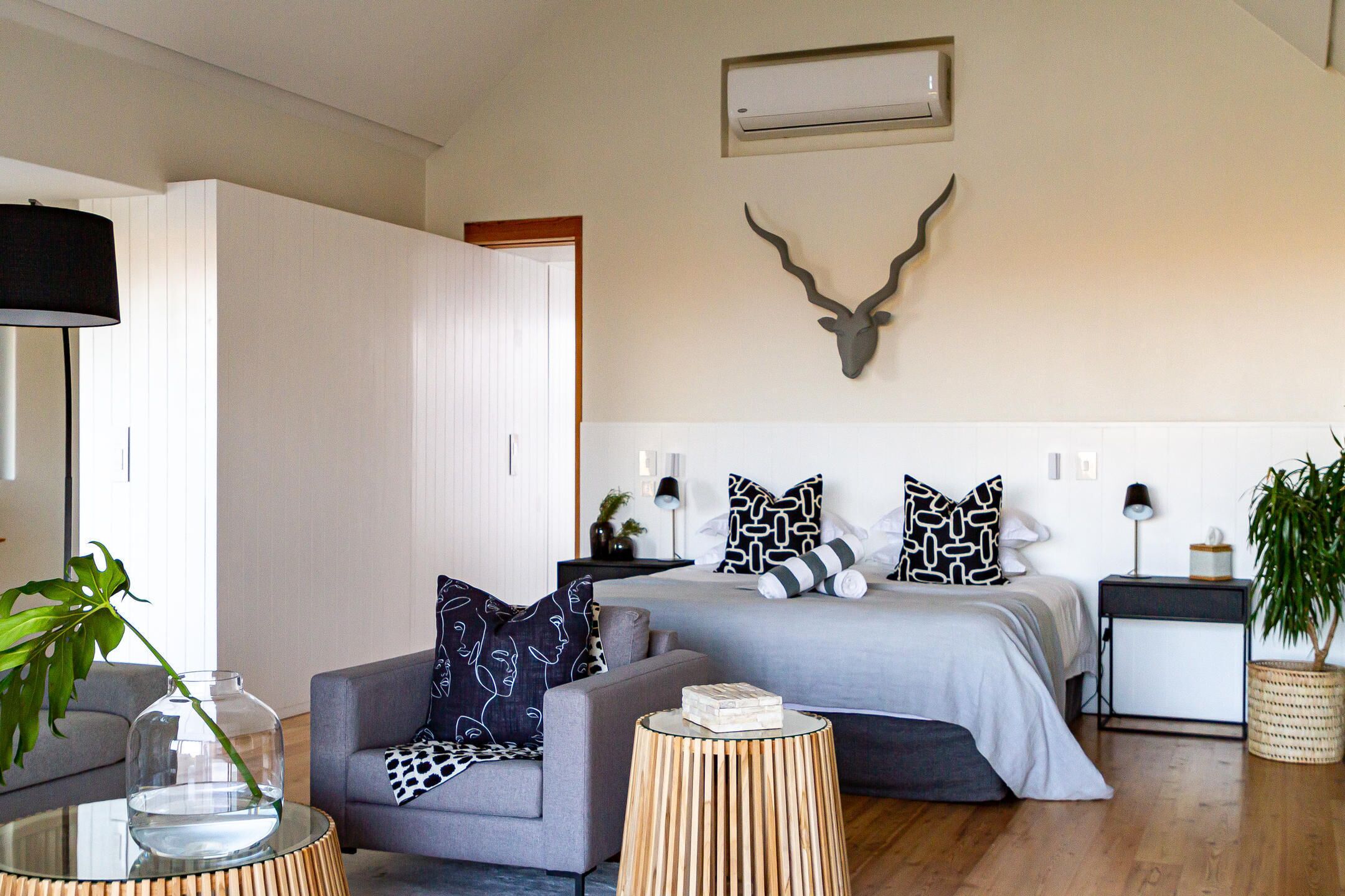 A modern bedroom with a bed, a grey sofa, a small round table, and a decorative wall piece.