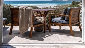 A wooden deck with a table and chairs overlooking a beach.