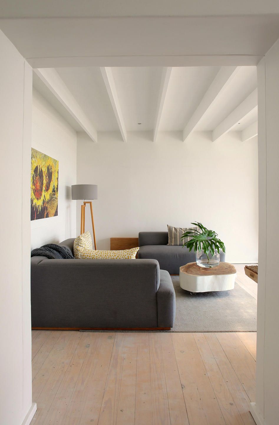 Una sala de estar moderna con un sofá gris, una lámpara de pie, una planta en maceta y un cuadro en la pared.