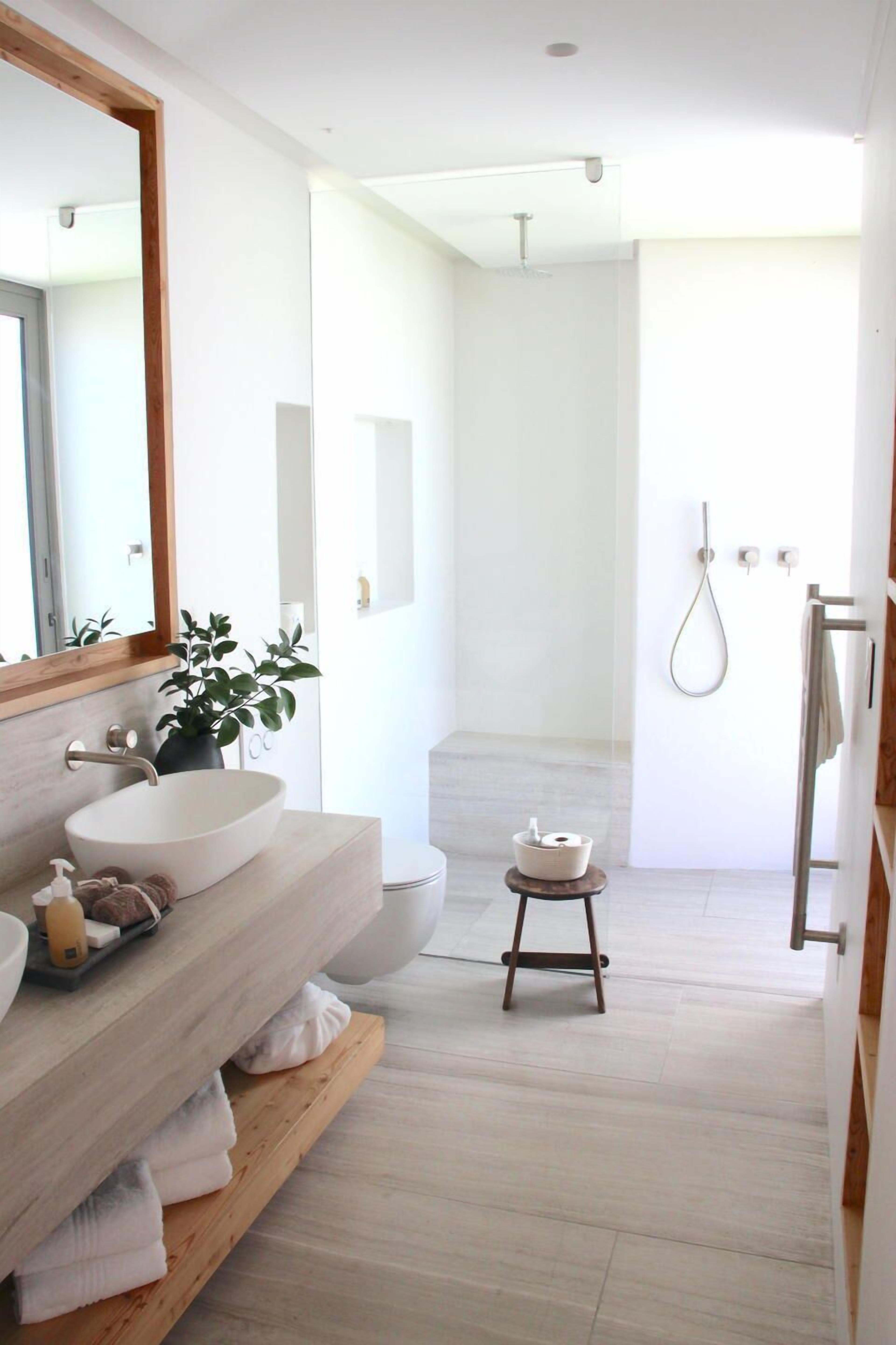 Un baño moderno con un espejo grande, un lavamanos blanco, un mueble de tocador de madera y un taburete pequeño.