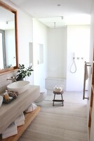 Un baño moderno con un espejo grande, un lavamanos blanco, un mueble de tocador de madera y un taburete pequeño.
