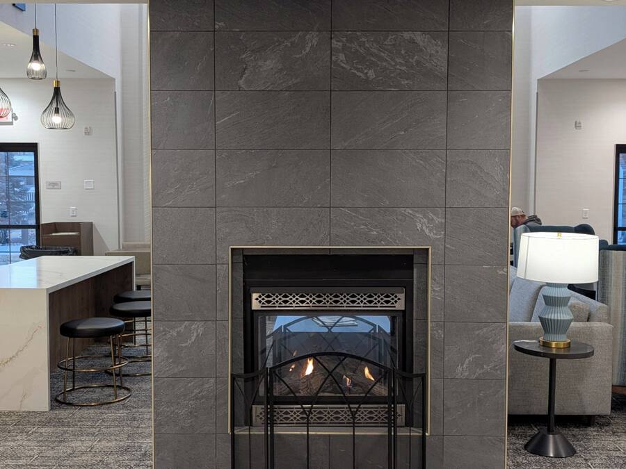 Un moderno vestíbulo de hotel con un mostrador de recepción de mármol, una chimenea y una zona de estar con lámpara y vistas al exterior.