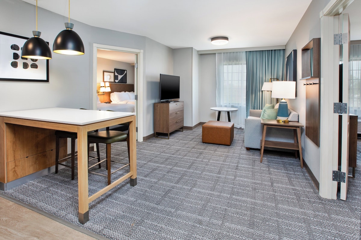 A modern hotel room with a dining area, a TV, a sofa, and a small table.