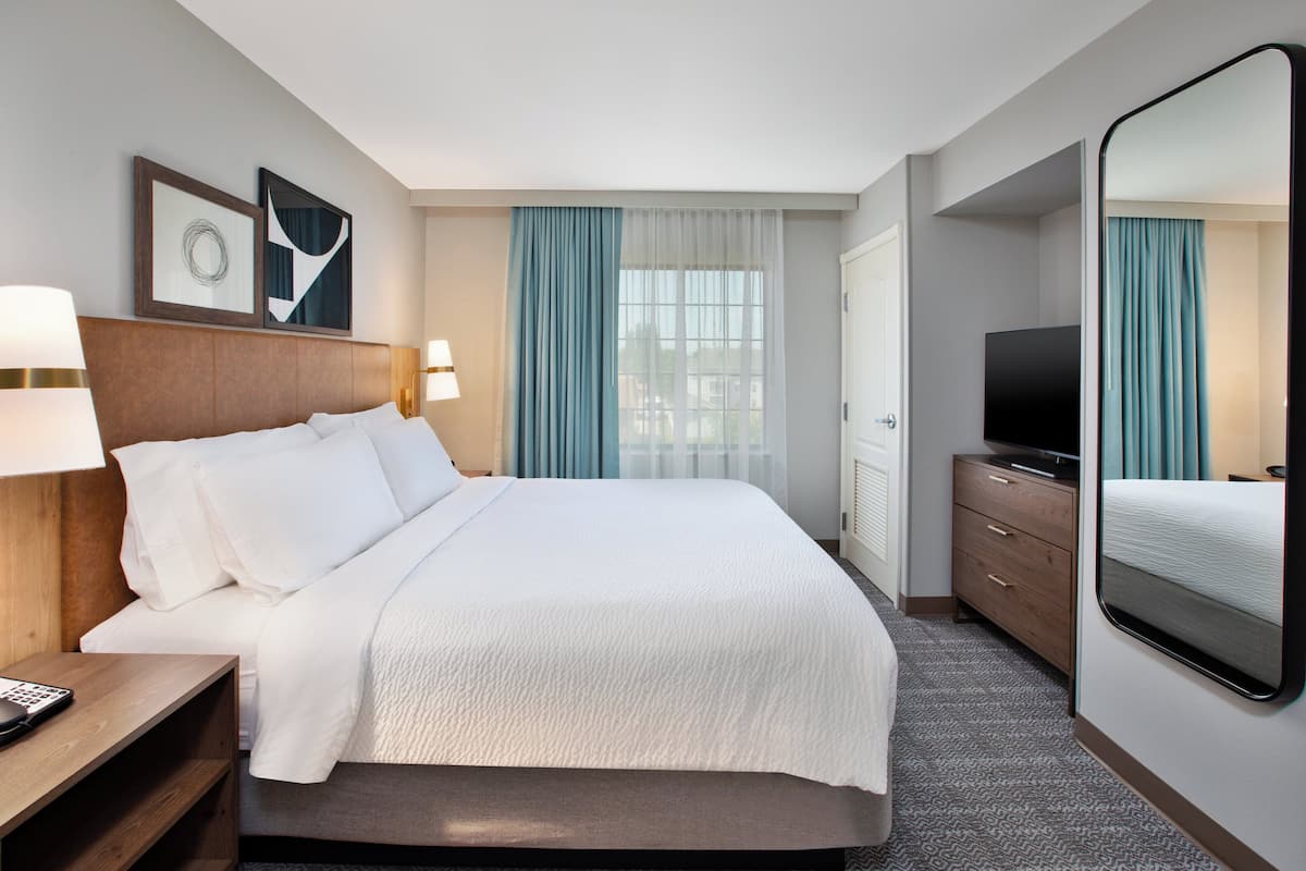 Ein Hotelzimmer mit einem großen Bett, einem Fernseher, einem Schminktisch und einem Spiegel.