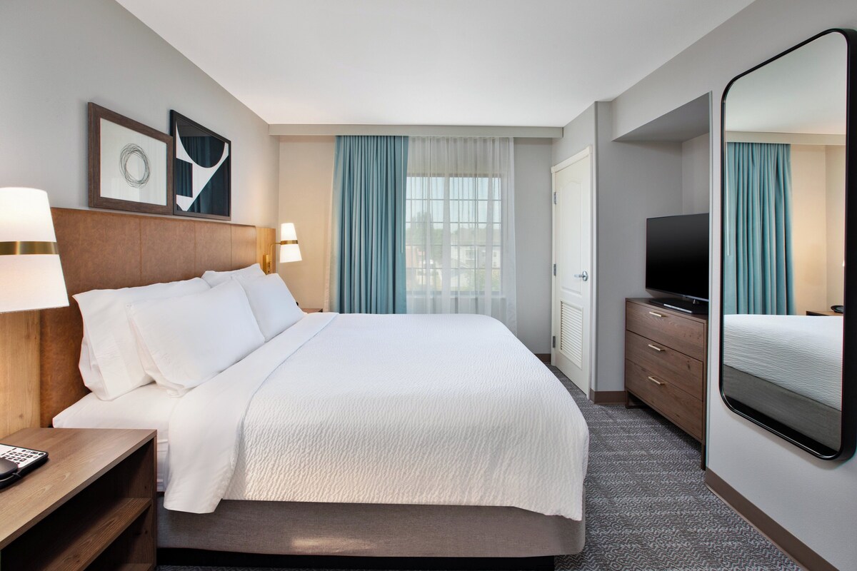 A hotel room with a large bed, a TV, a dresser, and a mirror.