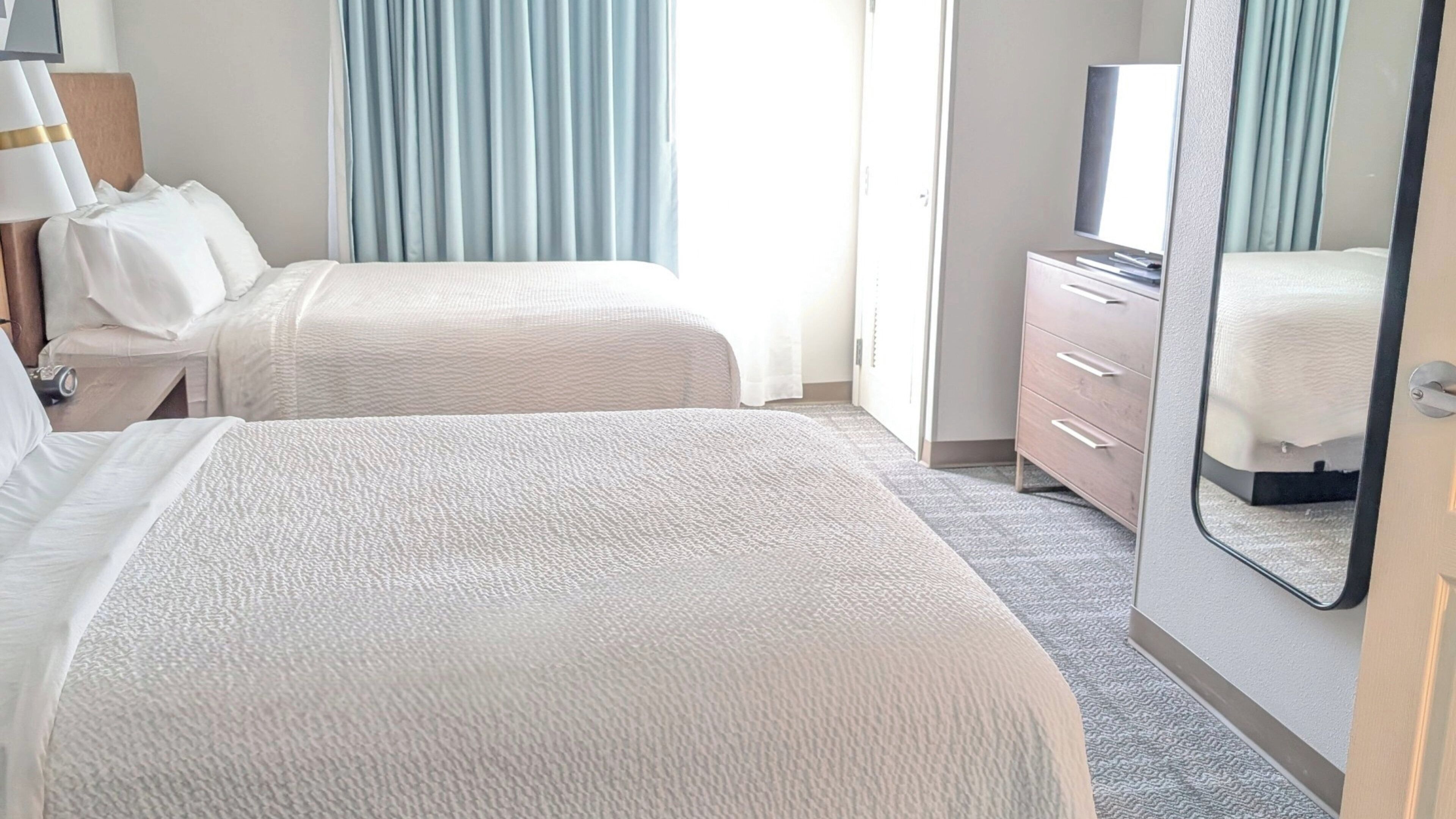 Ein Hotelzimmer mit zwei Betten, einem Schminktisch, einem Fernseher und einem Spiegel.
