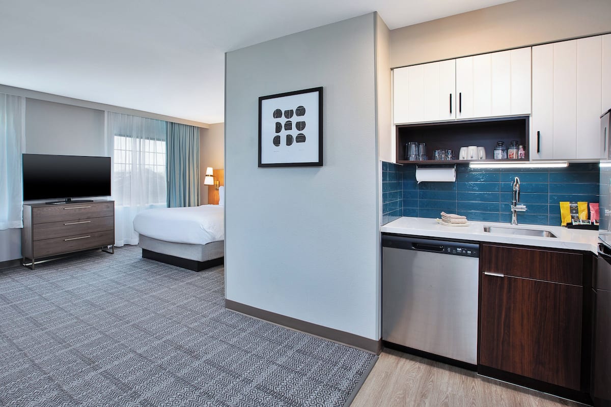 Ein modernes Hotelzimmer mit Flachbildfernseher, einem Bett, einer kleinen Küchenzeile und einem Badezimmer.