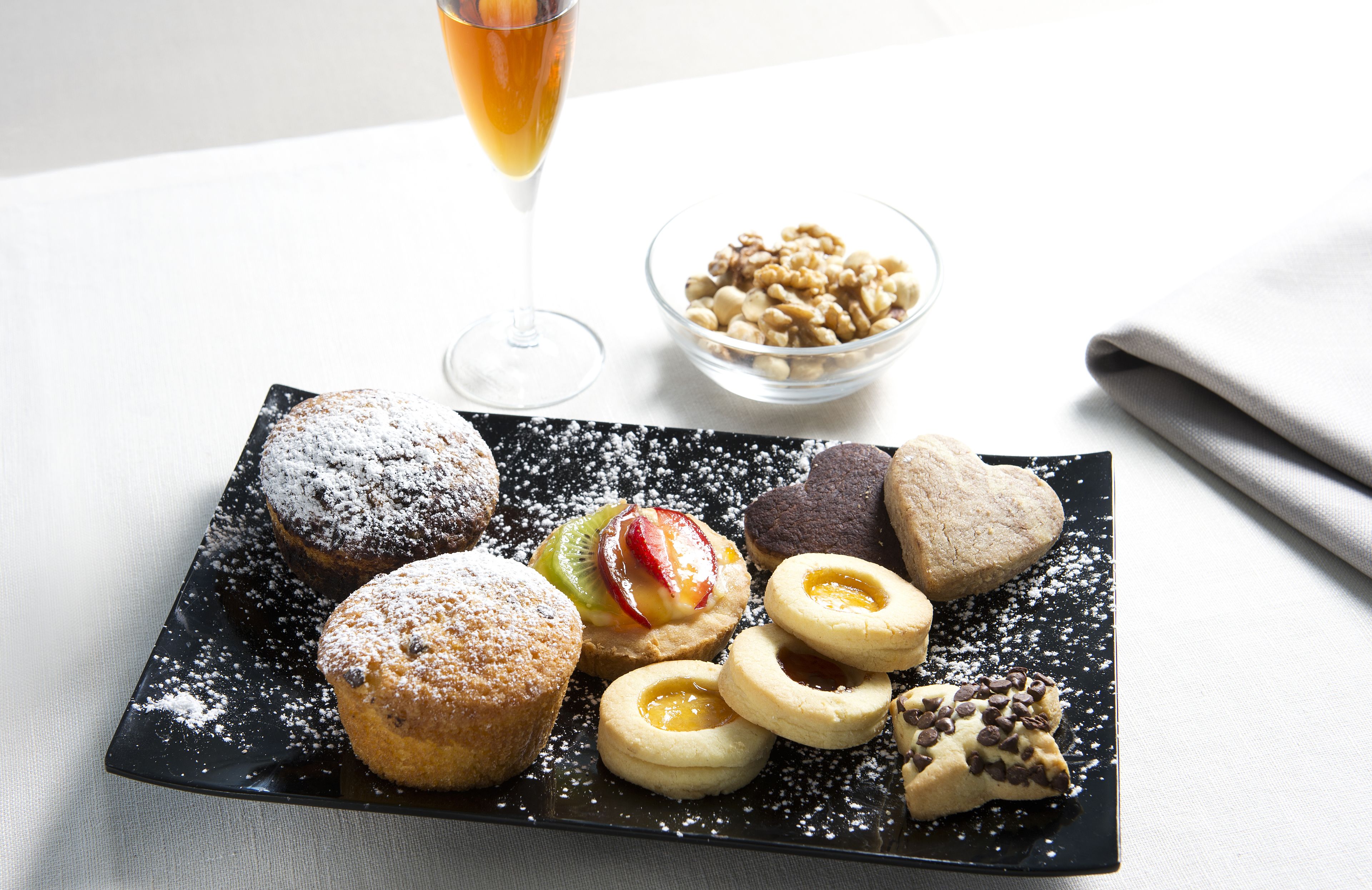 Variedad de pasteles en un plato negro, un vaso de bebida y un cuenco de nueces.