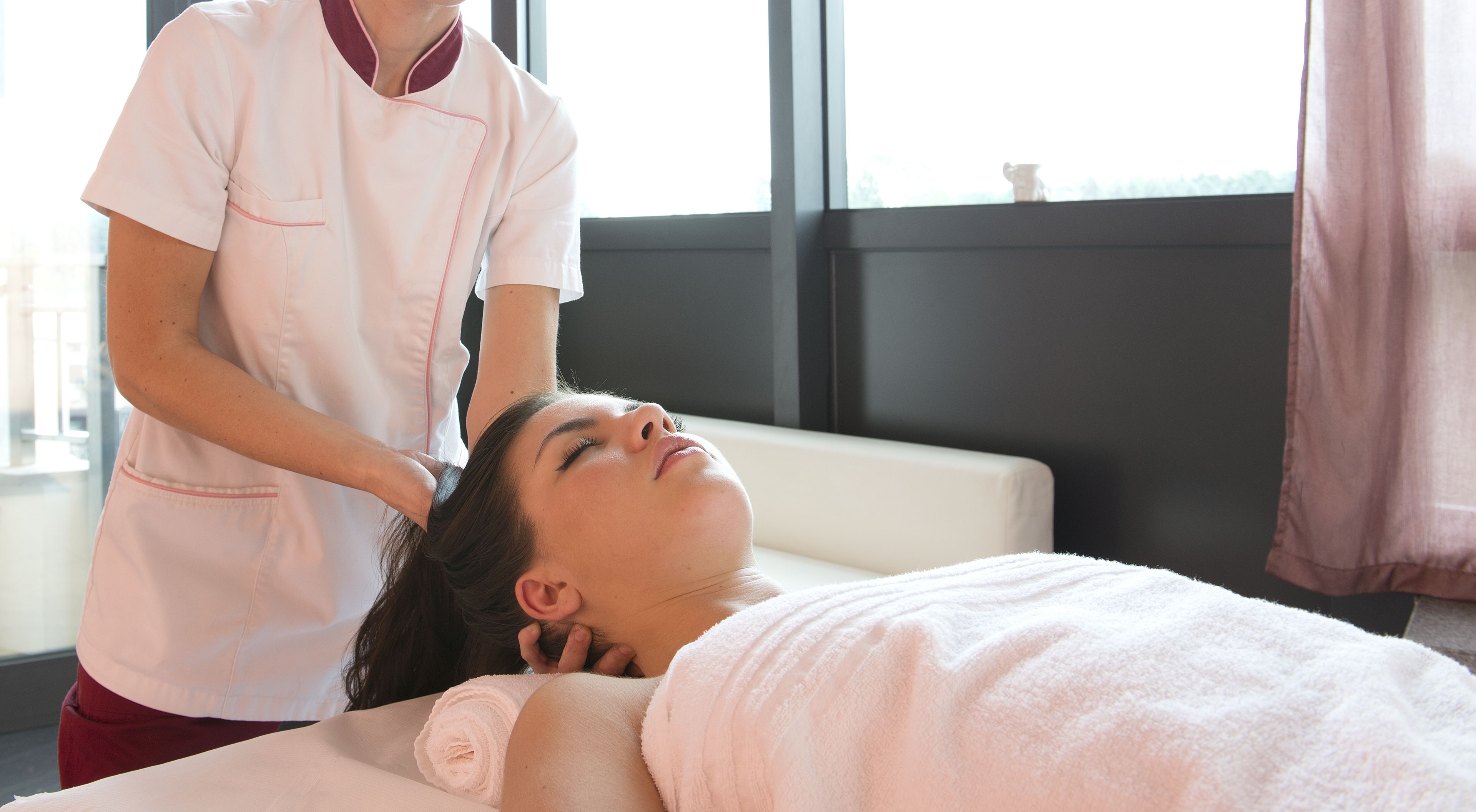 A person receiving a head massage in a room with a large window and a view of the outdoors.