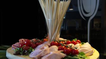 Una tabla de madera con fiambre en rodajas, tomates cherry y un manojo de espaguetis crudos.