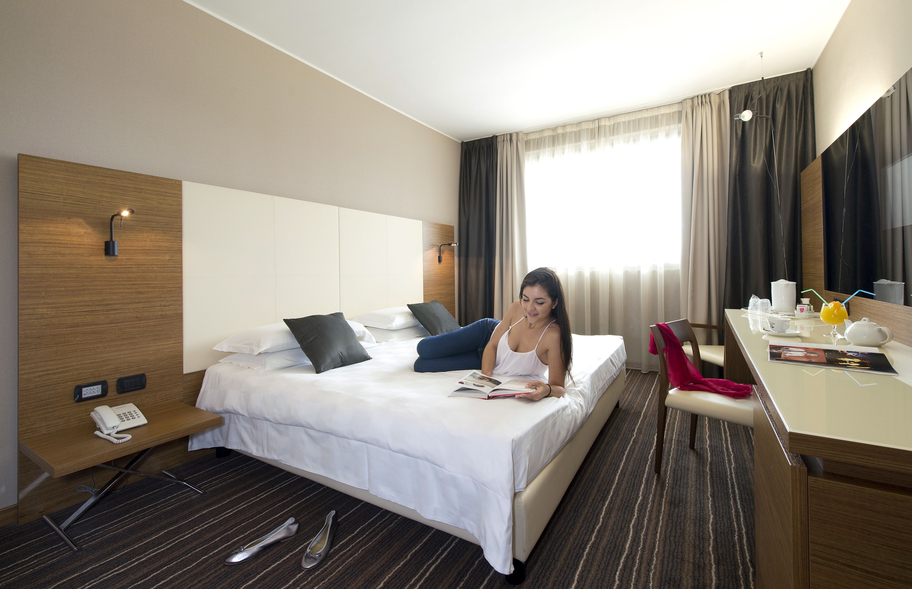 Habitación de hotel con cama, mesita de noche, escritorio y ventana con cortinas.