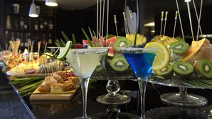 Una zona de bar con diversas bebidas y aperitivos, incluyendo cócteles con adornos de frutas y una selección de pasteles.