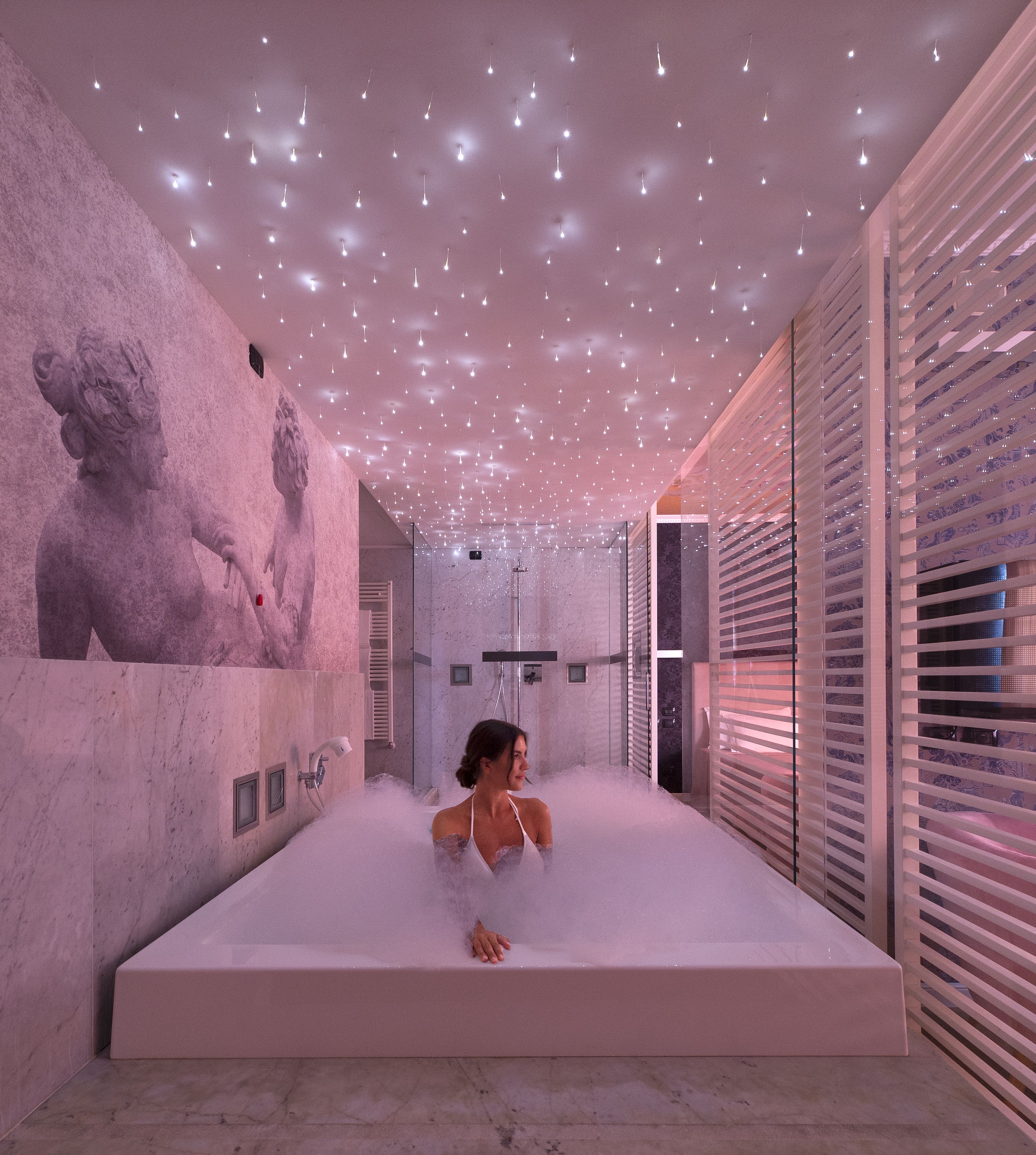 Un spa moderno con una bañera grande, una estatua en la pared y un techo con luces colgantes.