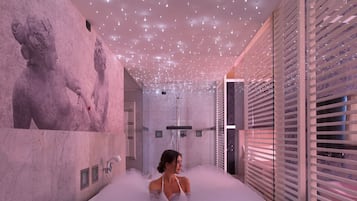 Un spa moderno con una bañera grande, una estatua en la pared y un techo con luces colgantes.