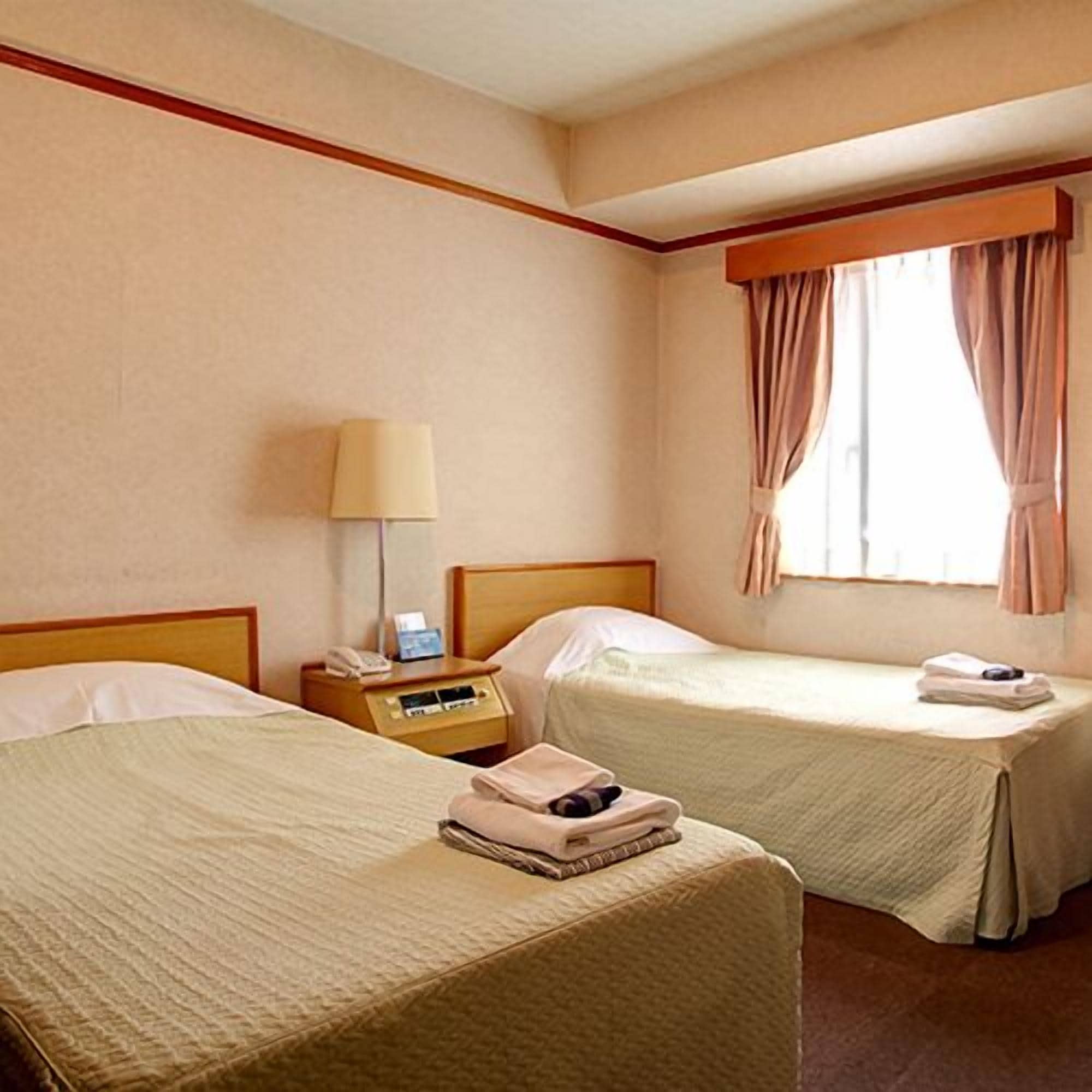 A hotel room with two beds, a nightstand with a lamp, and a window with curtains.