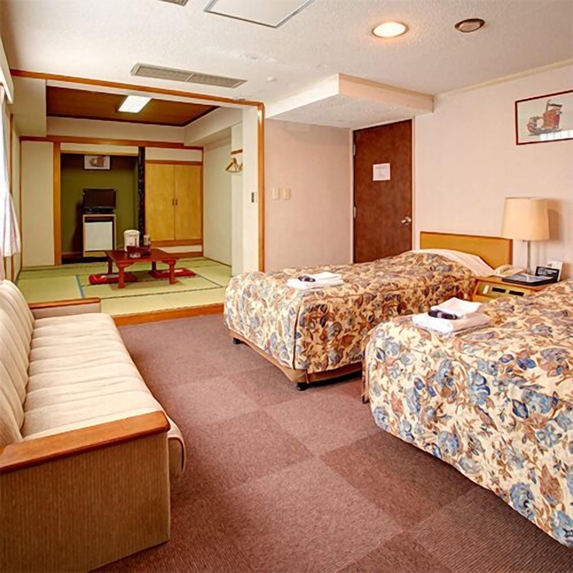 A hotel room with two beds, a sofa, a desk, a chair, and a television.