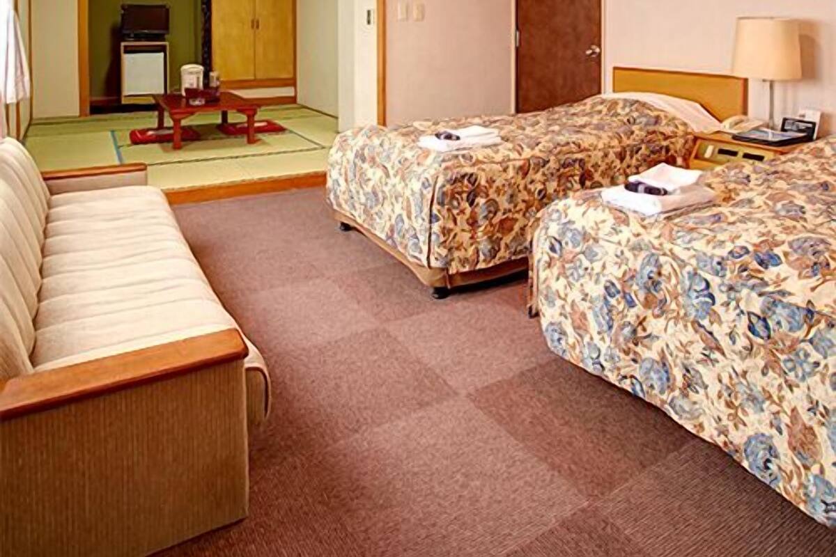 A hotel room with two beds, a sofa, a desk, a chair, and a television.