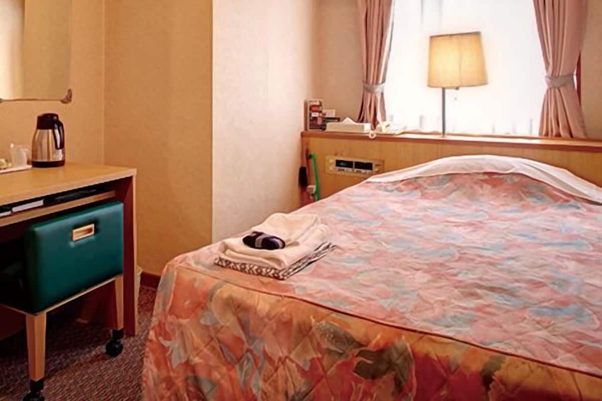 A hotel room with a bed, a desk with a coffee maker, a mirror, a window with curtains, and a lamp.