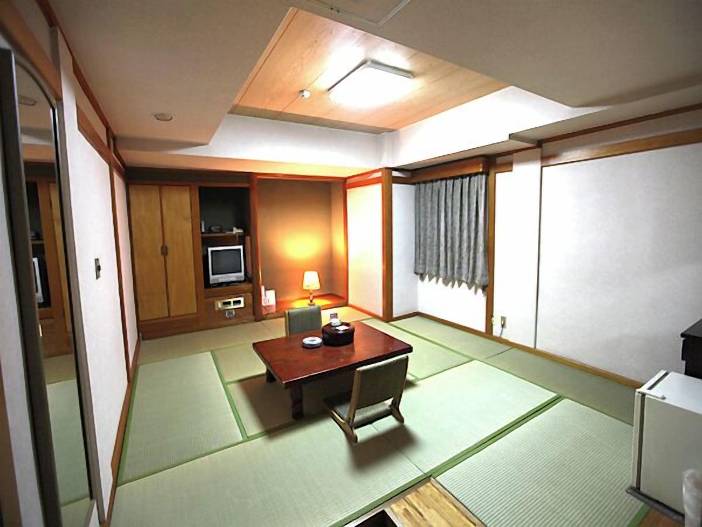 A traditional Japanese room with tatami flooring, a low table, a television, and a refrigerator.