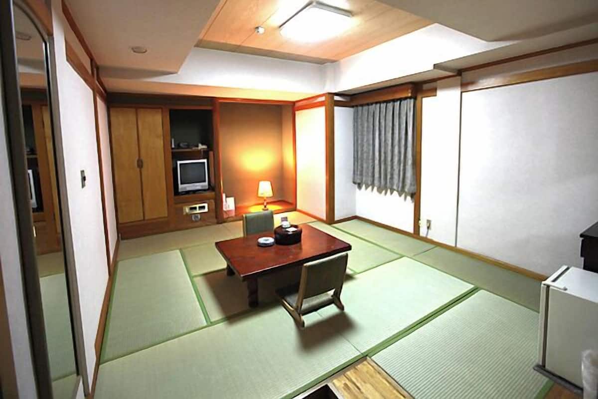 A traditional Japanese room with tatami flooring, a low table, a television, and a refrigerator.