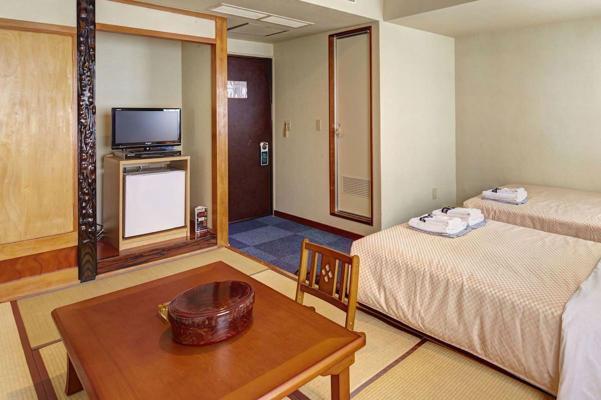 A hotel room with two beds, a small desk with a television, and a dining table.