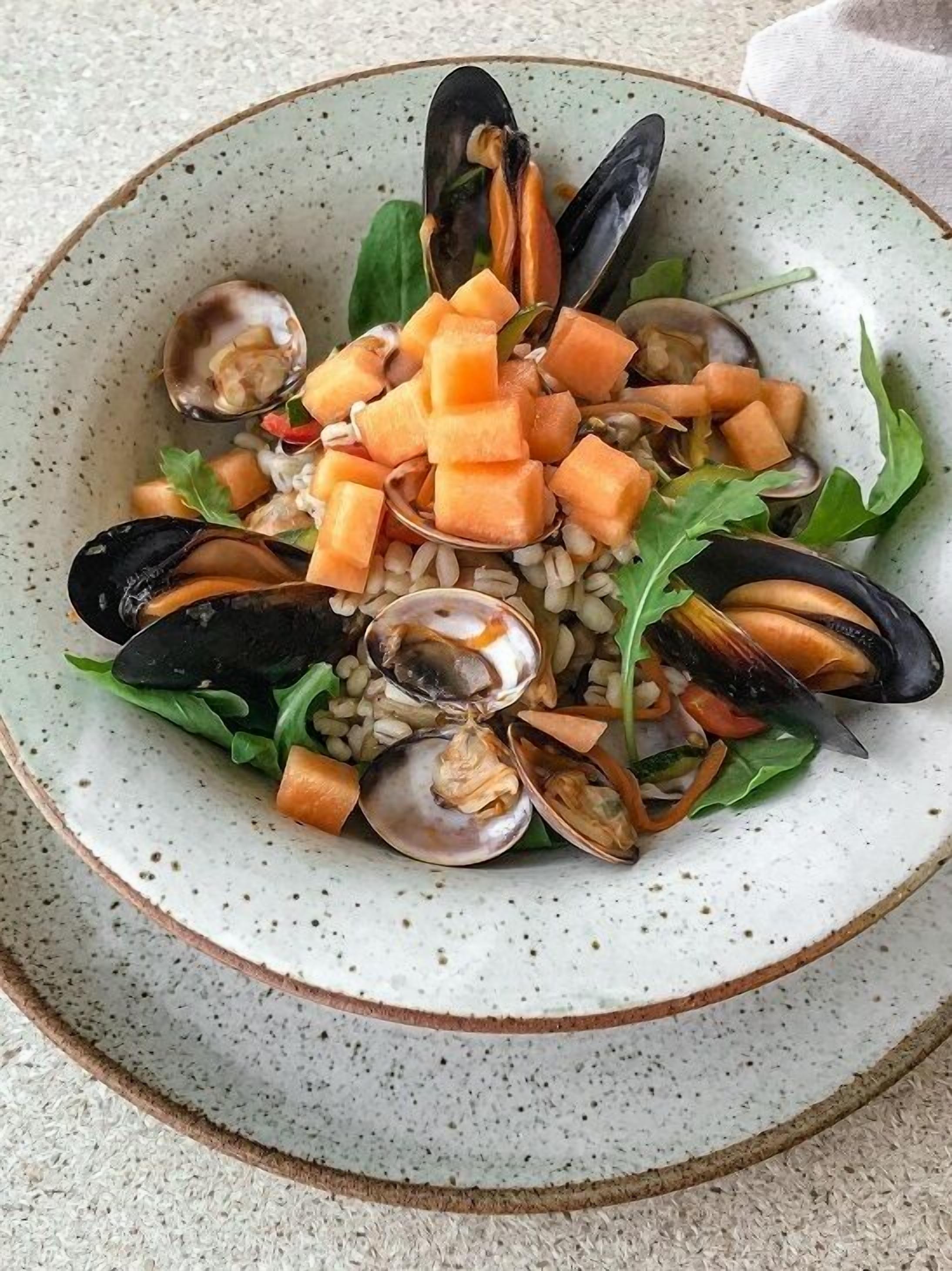 A bowl of seafood salad with mussels, carrots, and greens.