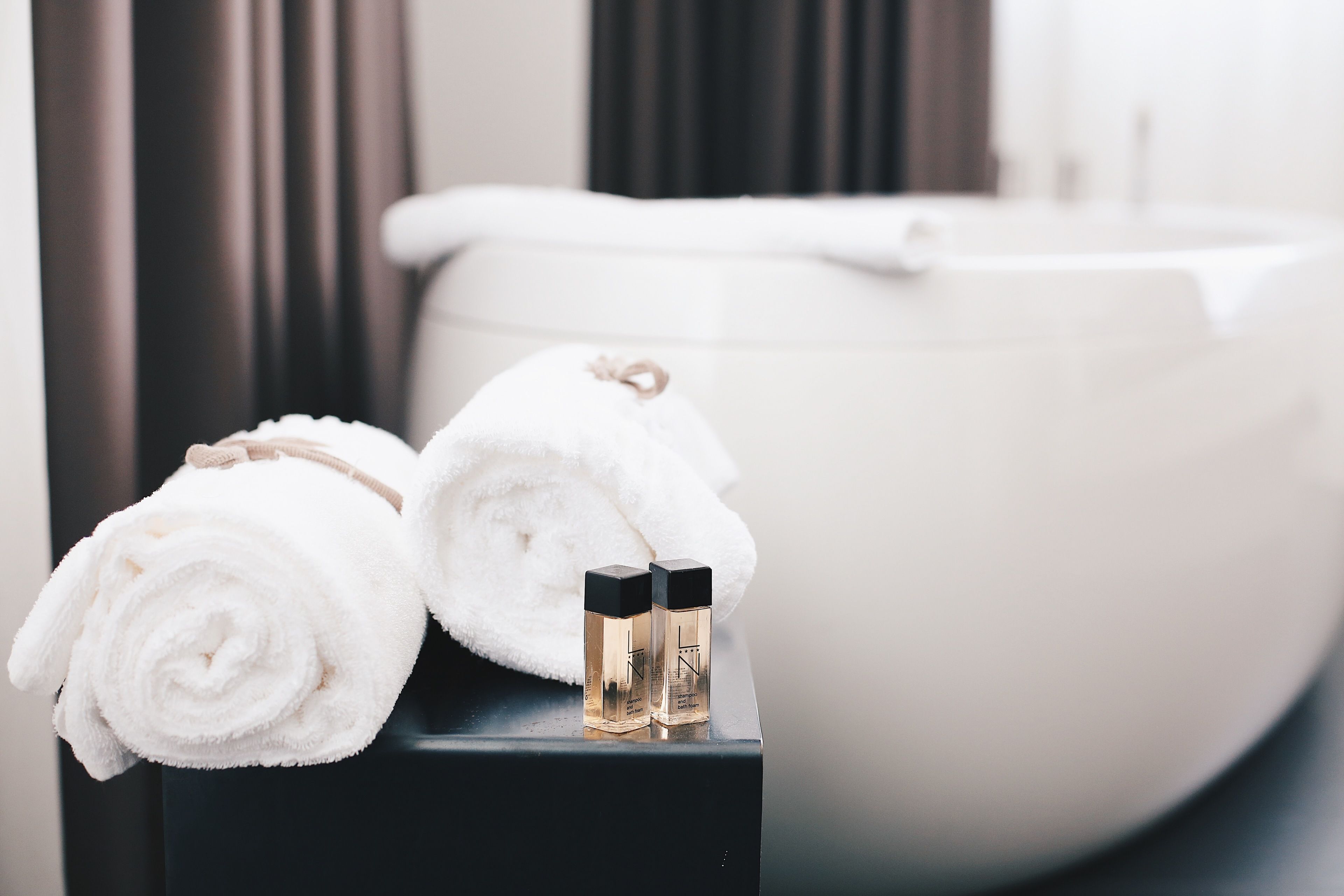 A bathroom with a bathtub, two rolled towels, and two small bottles on a black surface.